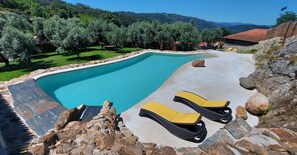 A swimming pool with a stone border, two yellow lounge chairs, and a view of a mountainous landscape. - For families who love nature and the countryside. (Celorico de Basto)