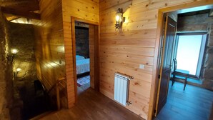 A wooden cabin interior with a stone wall, a bed, a radiator, and a window. - For families who love nature and the countryside. (Celorico de Basto)