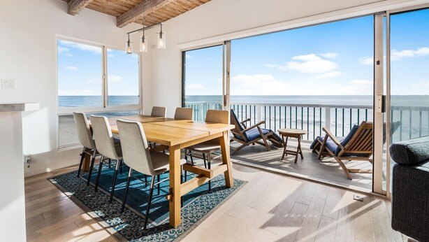 Een ruime kamer met een houten eettafel, stoelen en een balkon met uitzicht op de oceaan.