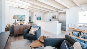 Een ruime woonkamer met een houten plafond, een eettafel en een keuken met koelkast en magnetron.