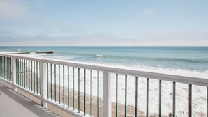 Uitzicht op het strand vanaf een balkon met een hekwerk, oceaan golven en een heldere lucht.