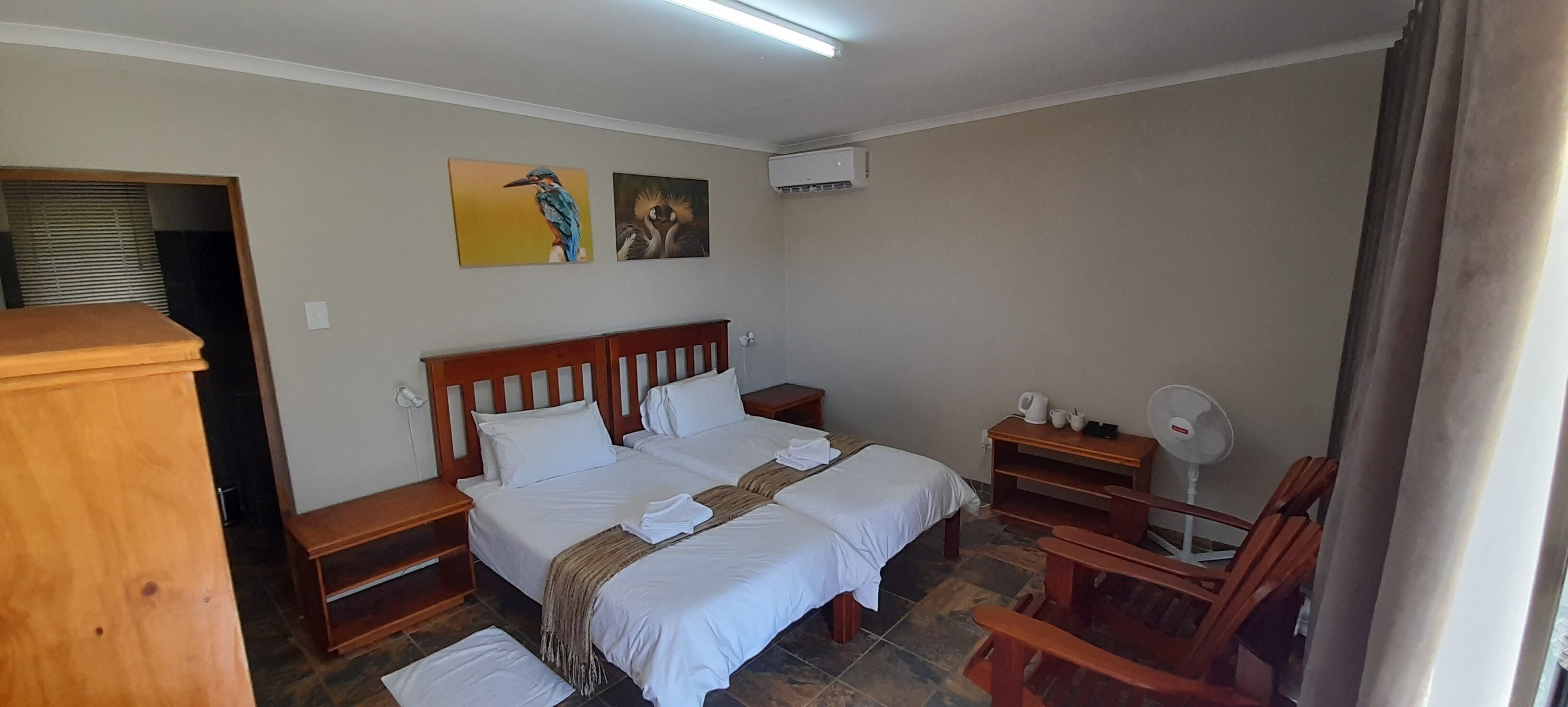 Une chambre à coucher avec un lit en bois, deux tables de chevet, une chaise, un ventilateur et des œuvres d’art accrochées au mur.