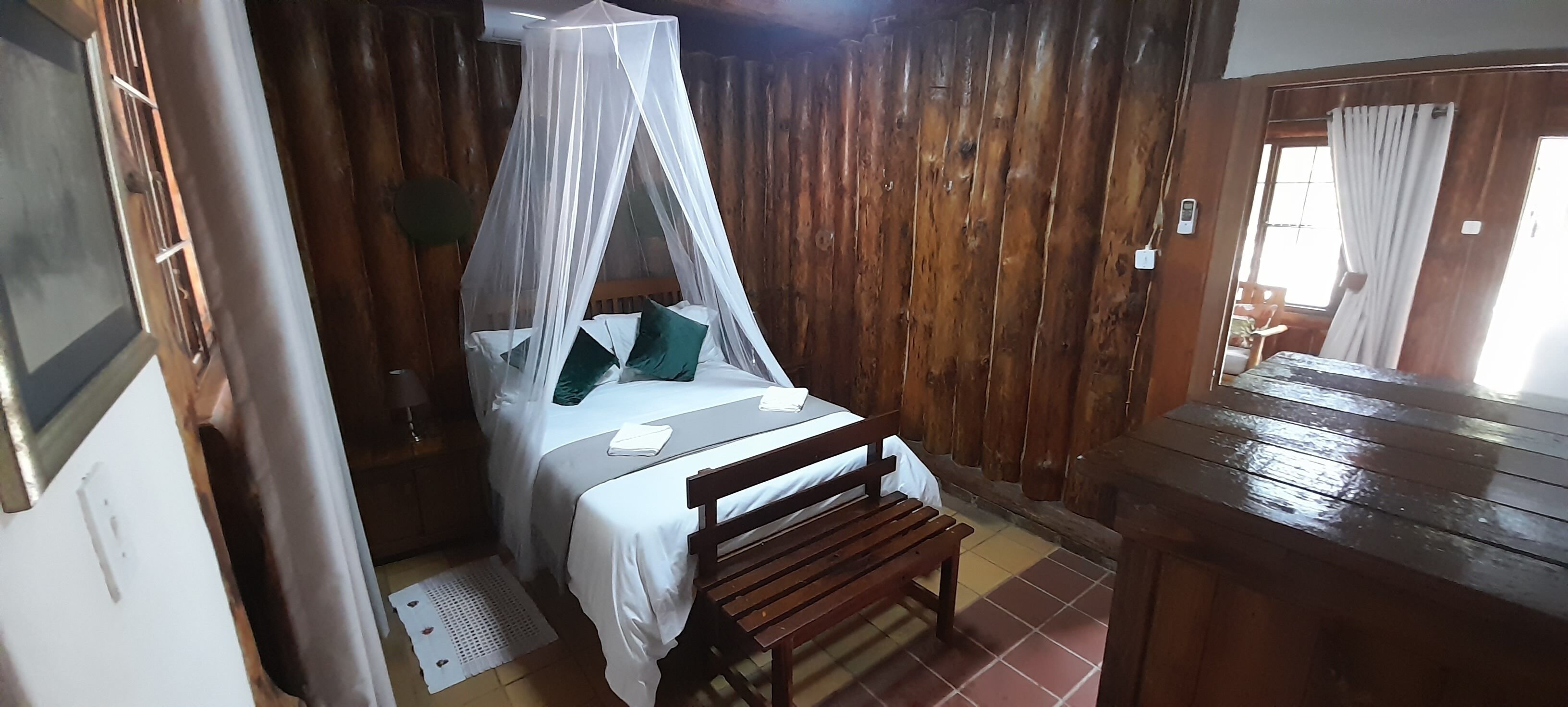 Una habitación con una cama bajo un dosel, paredes de madera, un banco y un aparador de madera.