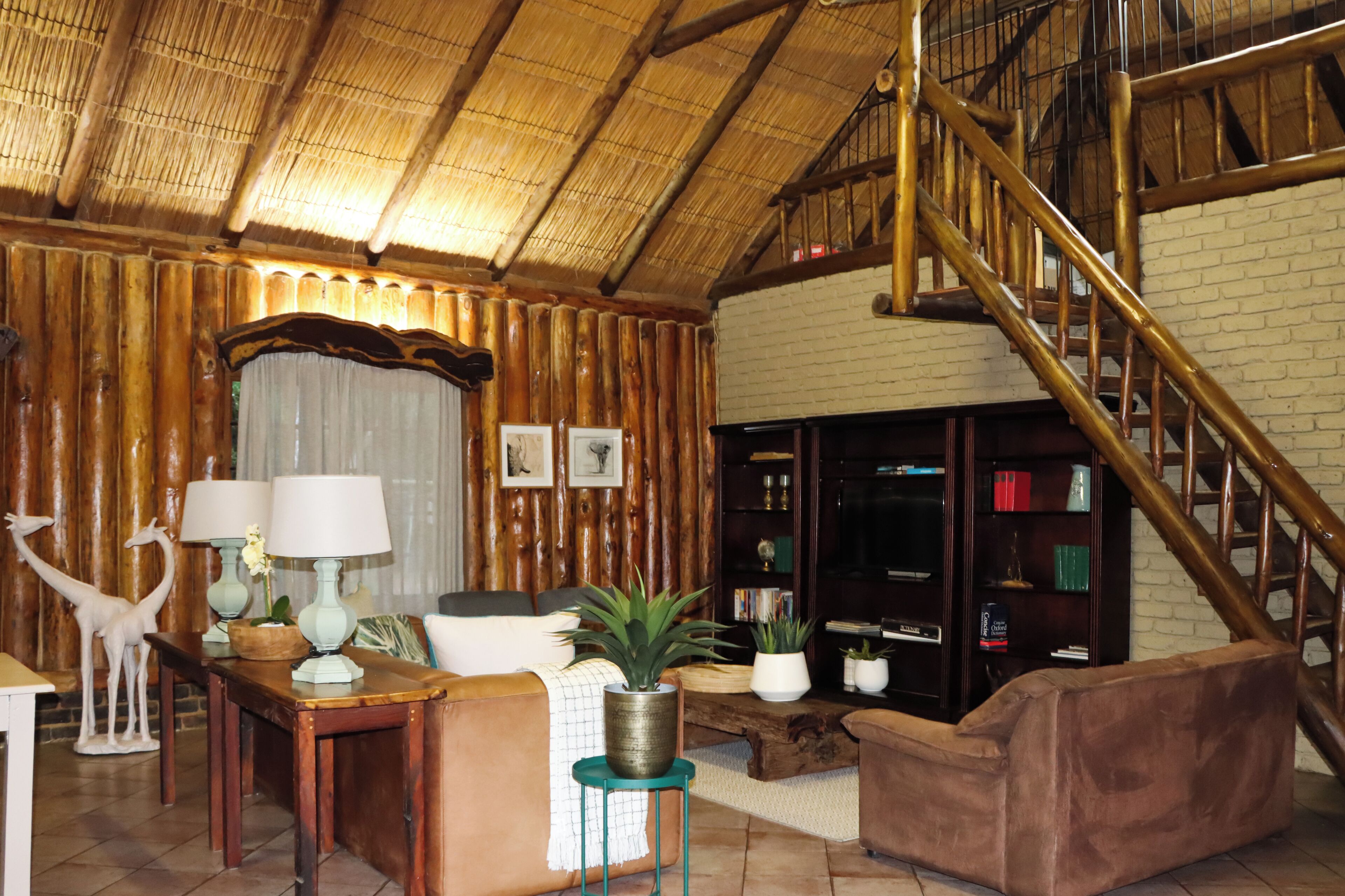 A rustic interior with a wooden ceiling, a staircase, a bookshelf, and a seating area.