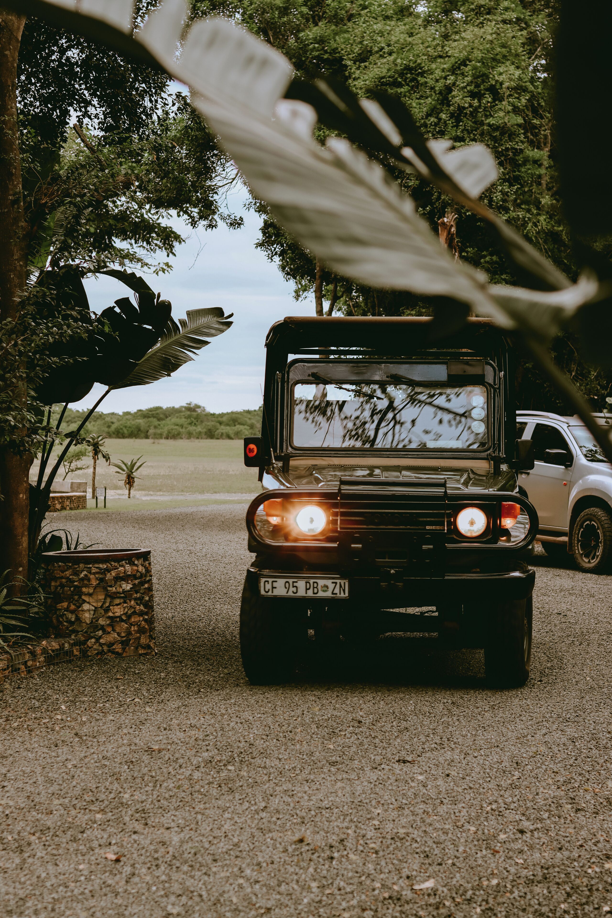 A black SUV parked on a gravel path with a stone planter and large leaves in the foreground.