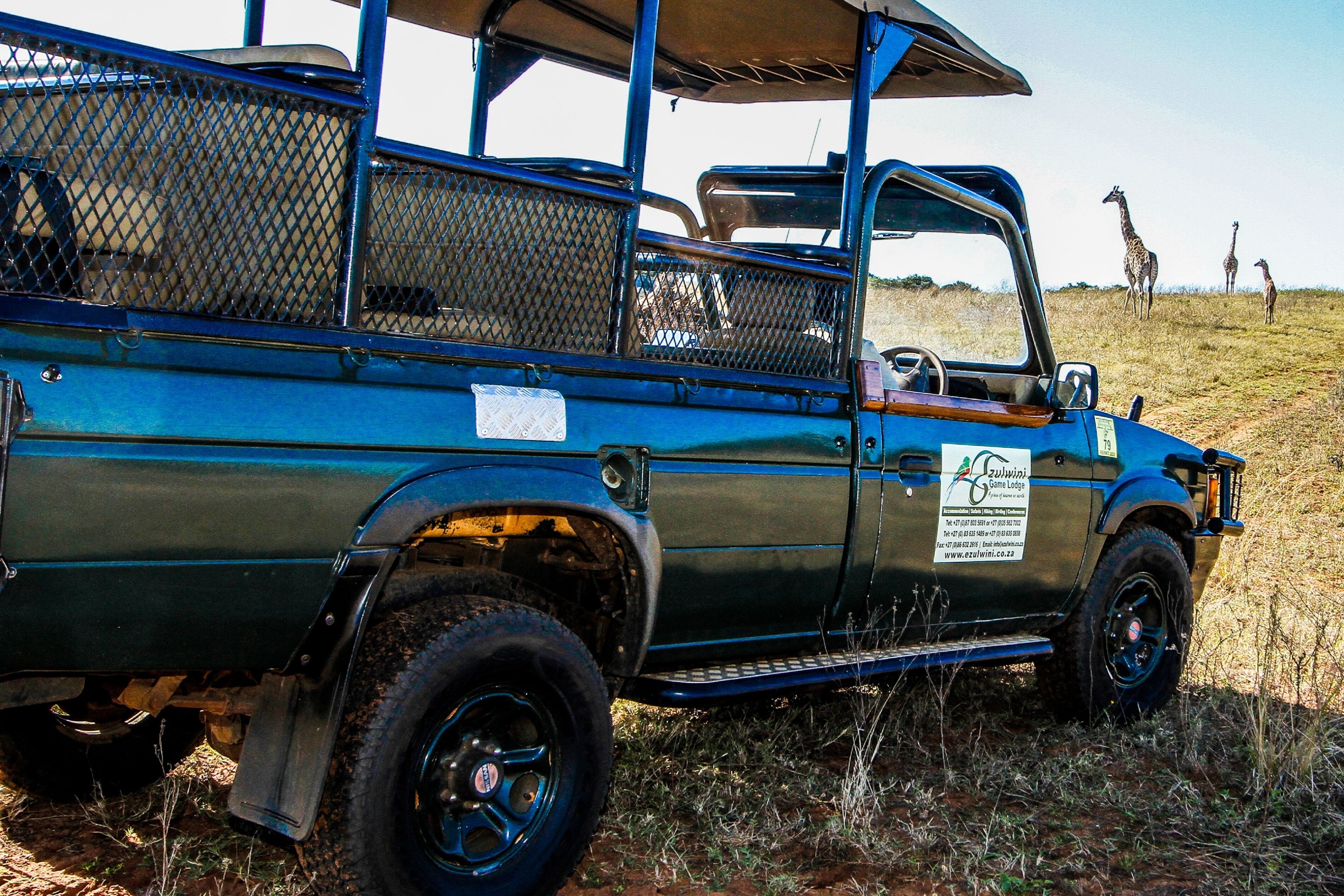Un véhicule de safari doté d’un dossier en treillis métallique et d’une enseigne publicitaire pour un lodge de safari.