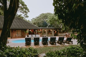 A poolside area with lounge chairs and a building with a sloped roof. - Ezulwini Game Lodge (Hluhluwe)