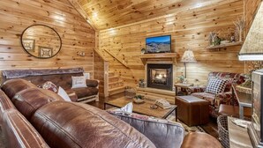 Interior acogedor de una cabaña de madera con chimenea, sofás de cuero y un televisor.