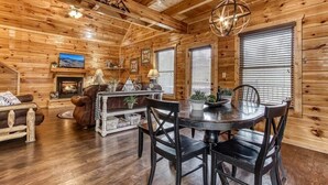 Interior acogedor de una cabaña con chimenea, paredes de madera, zona de comedor y televisor.