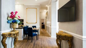 Un pasillo con comedor, televisor montado en la pared y muebles dorados ornamentados.