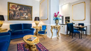 Amplia sala de estar con un sofá azul, un cuadro con marco dorado y una zona de comedor con mesa y sillas.