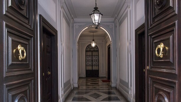 Un pasillo con puertas de madera oscura, suelo de mármol y una lámpara colgante.