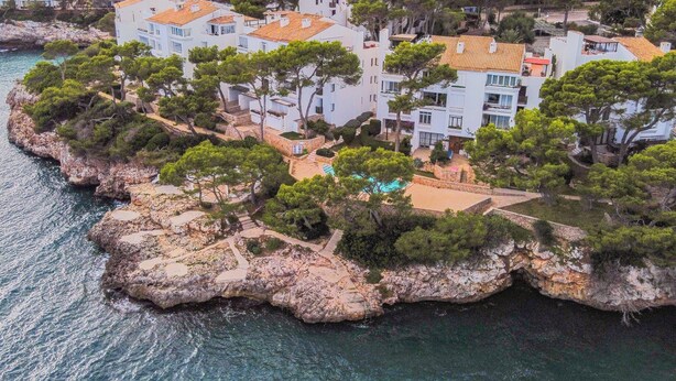 Una propiedad costera con varias edificaciones, un litoral rocoso y un mar azul cristalino.