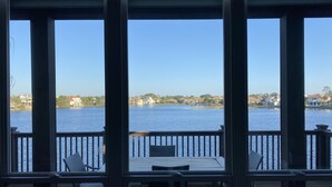A view from a covered deck with a table and chairs, overlooking a calm body of water and a distant shoreline with houses. - [Summer Deals on remaining dates] 3 min to Beach! Waterfront, Pool, Beach gear (Destin)
