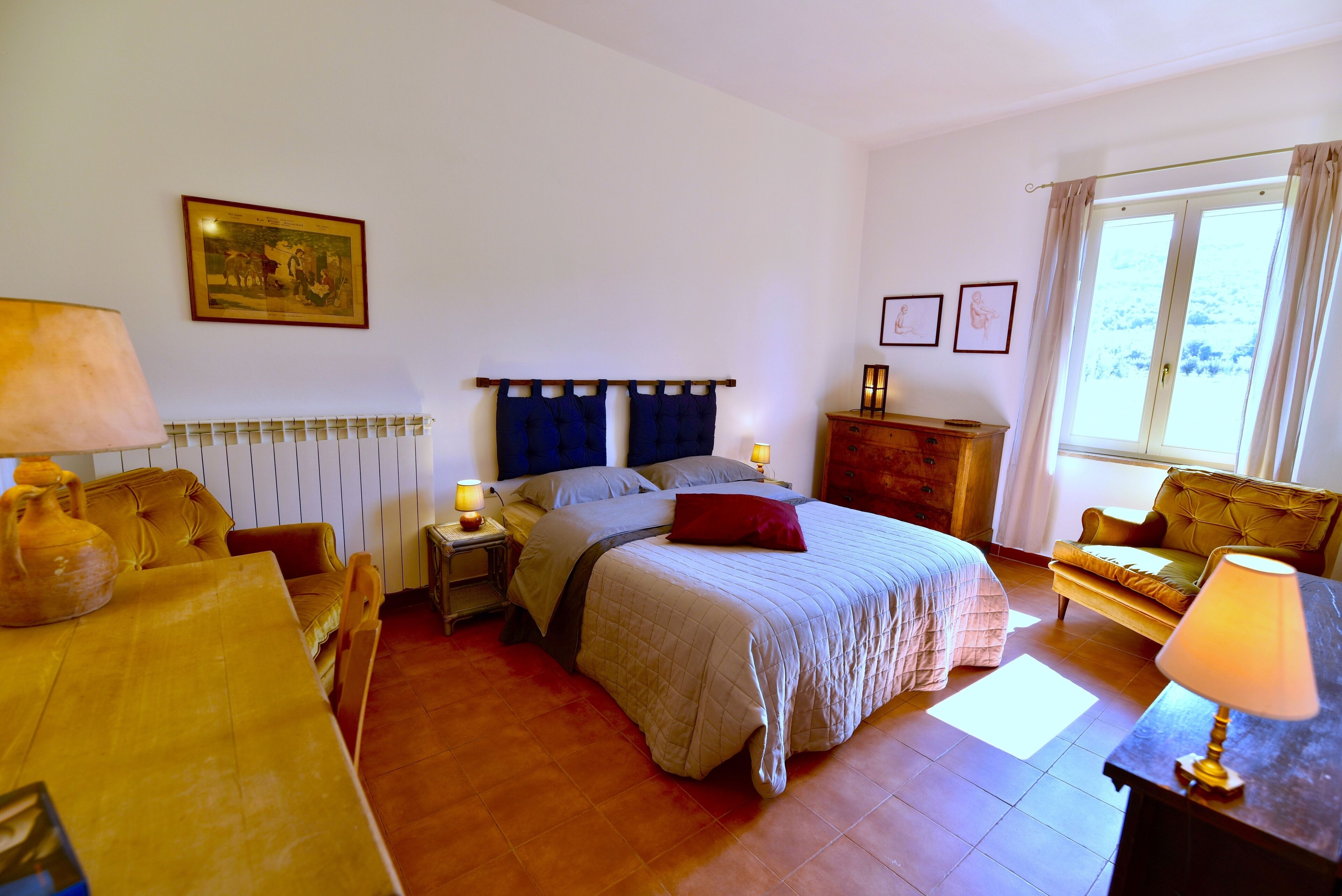 Une chambre à coucher comprenant un lit, des tables de chevet, un canapé, une lampe, un radiateur et une fenêtre avec des rideaux.