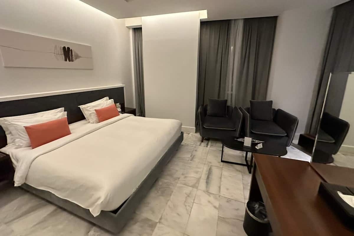 A modern hotel room with a large bed, a desk, two chairs, and a large mirror.