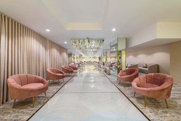 Un vestíbulo de hotel con un suelo reflectante en el centro, sillas tapizadas en tonos rosados y un candelabro.