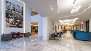 A spacious lobby with a marble floor, a blue sofa, a dining area with blue chairs, and a large abstract painting on the wall.