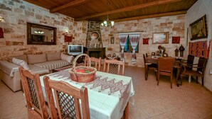 A rustic dining area with a wooden table, chairs, and a stone wall backdrop. - Anthis Cottage (Malevizi)