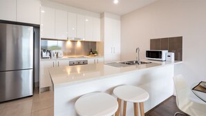 A modern kitchen with white cabinetry, stainless steel appliances, and a central island with stools. - Blue Vista - a modern apartment (Gerringong)