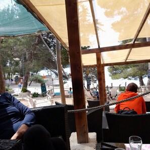 Un espace extérieur aménagé avec des chaises et des tables en osier, protégé par un auvent.