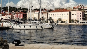 Ein Yachthafen mit mehreren Segelbooten, einer Uferpromenade und Gebäuden mit roten Dächern im Hintergrund.