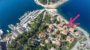 Une vue aérienne d’une zone côtière comprenant un port de plaisance, des immeubles résidentiels et une grande flèche rose bien visible, indiquant un endroit précis.