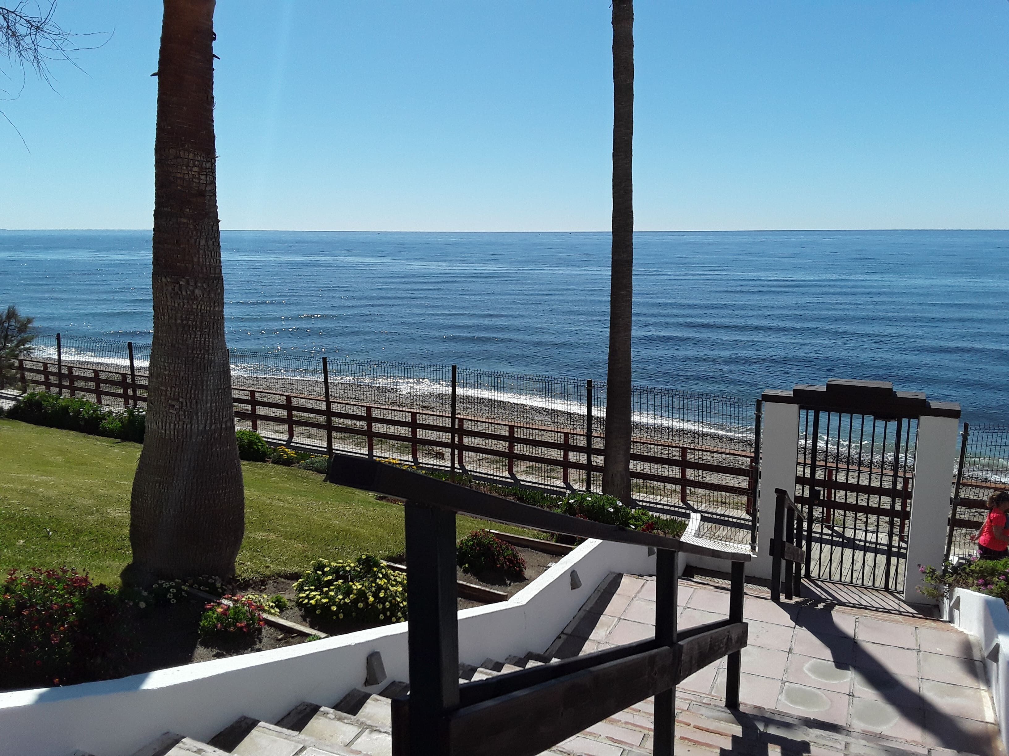 Vista costeira com uma escadaria que leva a uma área cercada, com vista para a praia.