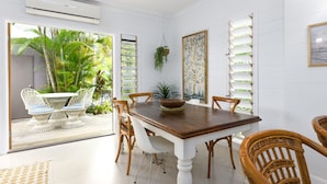 Un coin repas avec une table en bois et des chaises en osier, une plante suspendue et une vue sur la verdure environnante.