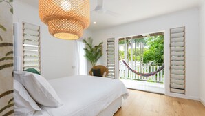 Une chambre avec un lit, un ventilateur de plafond et une vue sur une clôture blanche et de la verdure à l’extérieur.