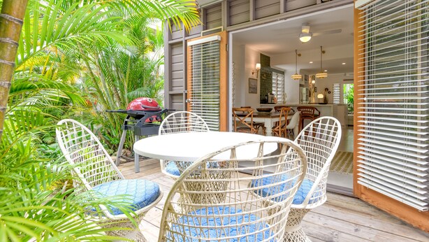 Une terrasse extérieure aménagée avec des meubles en osier, un barbecue et une végétation luxuriante.
