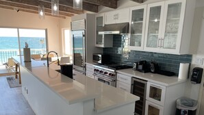 Une cuisine moderne avec des meubles blancs, un grand îlot central et une vue sur l’océan.