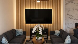 Un salon moderne doté d’un grand téléviseur à écran plat, de deux canapés ornés de coussins à motifs, d’un mur d’accent en bois et d’une cheminée en marbre.