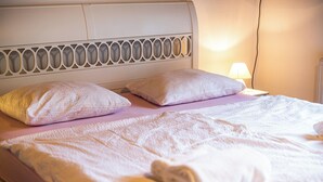 Ein ordentlich bezogenes Bett mit einem weißen Kopfteil, zwei Kissen und einem aufgerollten Handtuch.