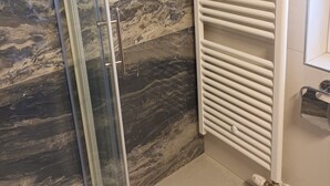 Ein Badezimmer mit Duschkabine aus Glas, Marmorwand und weißem Handtuchhalter.