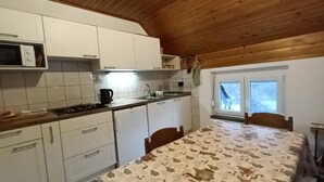 Eine Küche mit weißen Schränken, einer Mikrowelle, einem Herd und einem Spülbecken. Ein Fenster bietet einen Blick ins Freie.