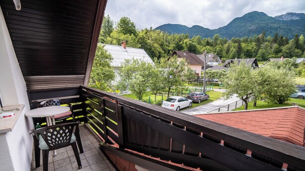 Ein Balkon mit Tisch und Stuhl, mit Blick auf eine Wohngegend mit Häusern und einem Berg im Hintergrund.