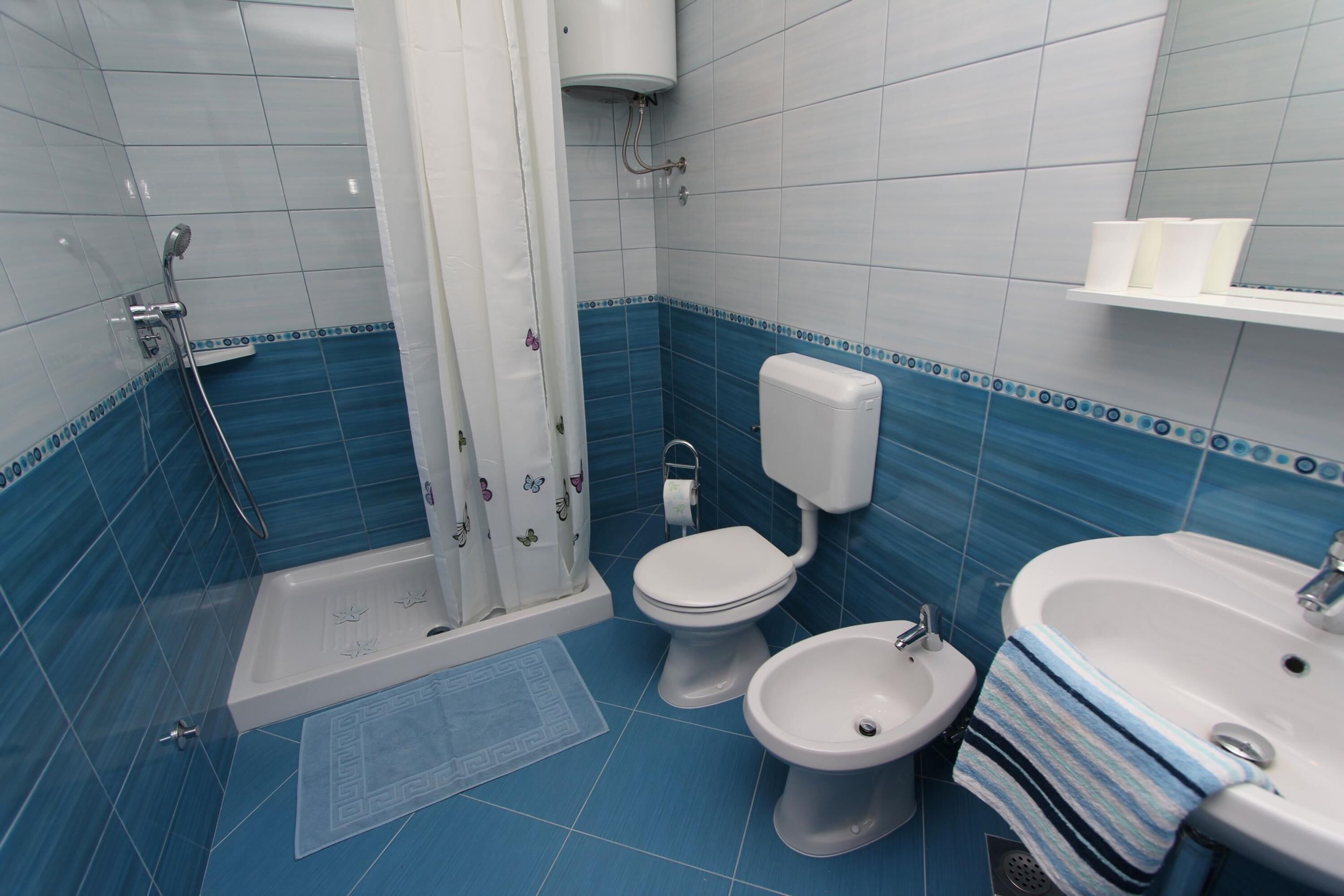 A bathroom with a shower, toilet, bidet, and sink.