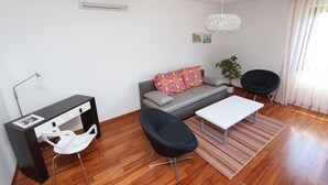A modern living room with a sofa, two black chairs, a white table, and a desk with a lamp. - Apartment Mitton 2 (Rovinj)