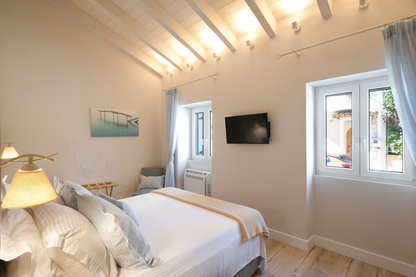 A bedroom with a bed, a TV, a window, and a painting on the wall.