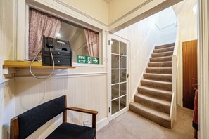 A hotel room with a fire exit sign, a telephone, and a chair. - House - Sleeps 6 & Paid off Site Parking Available (Minehead)
