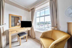 A hotel room with a wooden desk, a chair, a large window with curtains, and a view of the outside. - House - Sleeps 6 & Paid off Site Parking Available (Minehead)