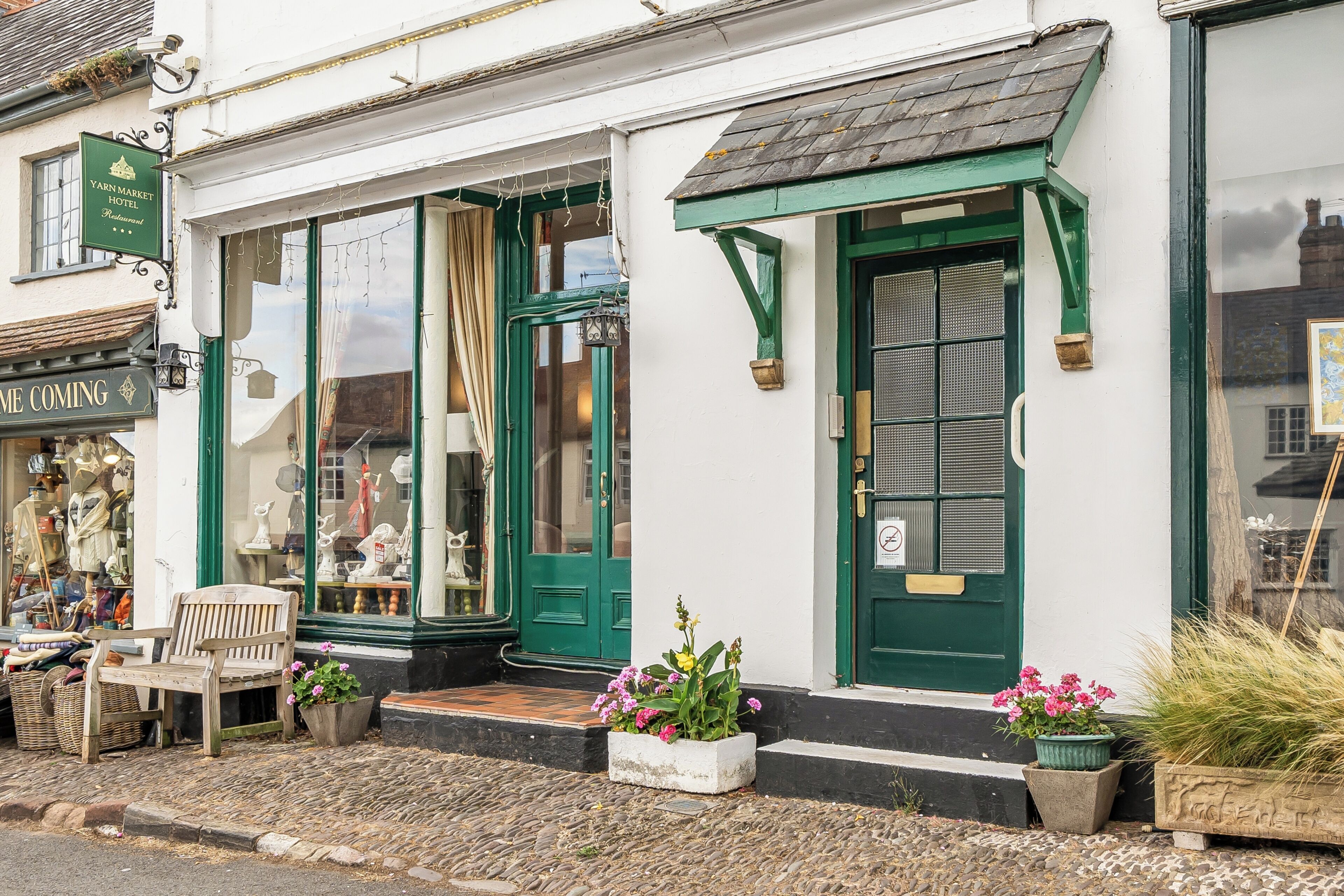 A traditional building with a green door and windows, a bench outside, and a sign for Yarn Market Hotel.