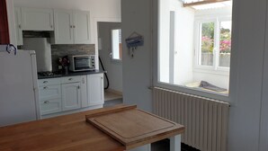 A kitchen with white cabinets, a microwave, a toaster, and a wooden table. - Pretty villa in Trévignon, 2 steps from the beach and port (Trégunc)