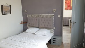 A neatly made bed with white bedding in a room with a grey wall, a framed picture, and a door leading to another room. - Pretty villa in Trévignon, 2 steps from the beach and port (Trégunc)