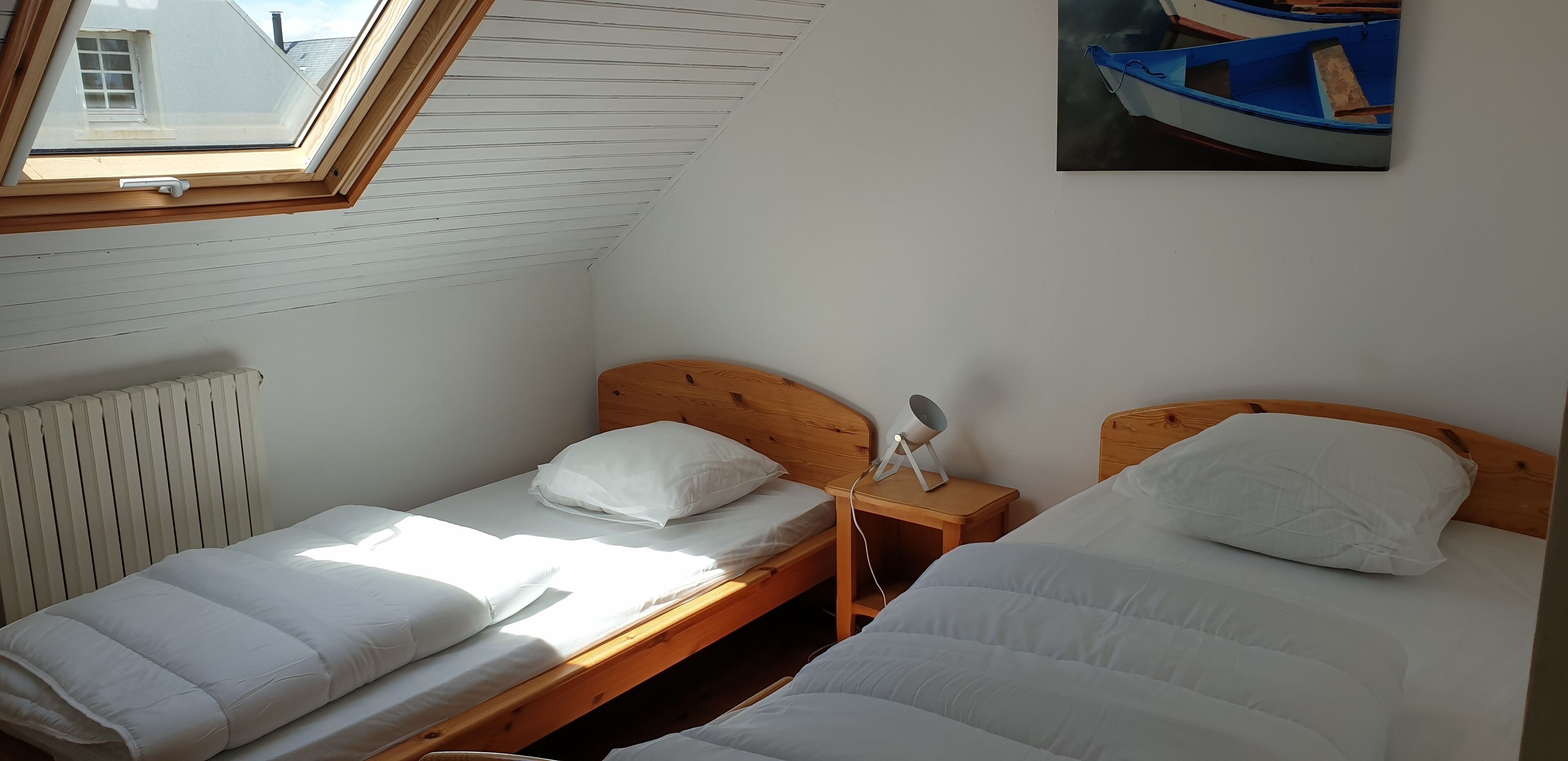 Un dormitorio con dos camas individuales, un tragaluz, un radiador y un cuadro de un barco en la pared.