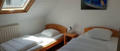 Un dormitorio con dos camas individuales, un tragaluz, un radiador y un cuadro de un barco en la pared.