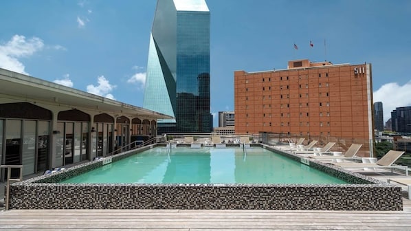 A rooftop pool with lounge chairs, a modern building with a unique shape, and a classic building with a grid pattern. - Bold CozySuites w/pool, gym, roof #3 (Dallas)