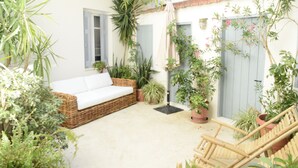 Un espace extérieur accueillant, aménagé avec un canapé en osier, un fauteuil en bois et divers pots de plantes.