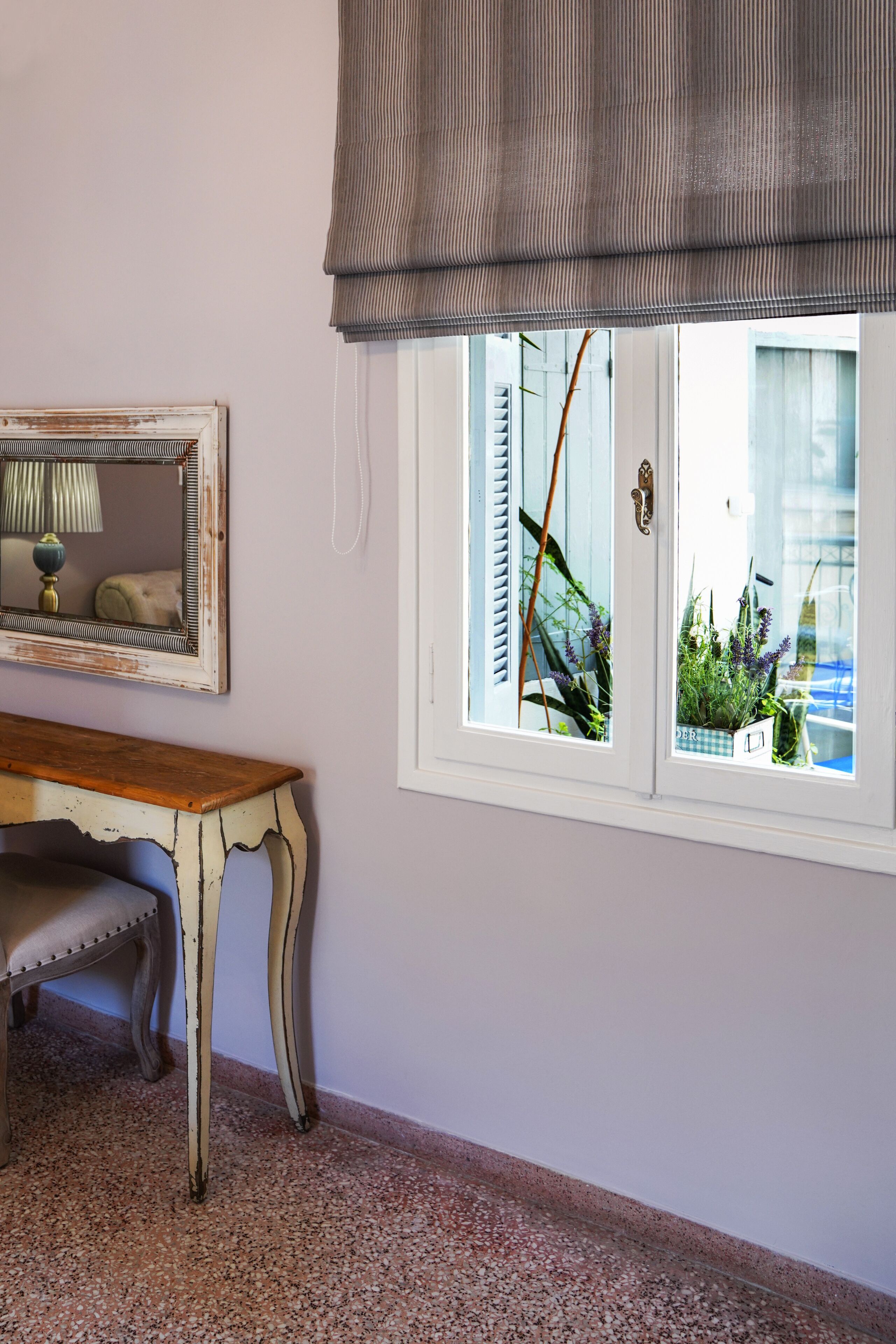 A room with a white-framed window, a wooden table, a bench, and a mirror on the wall.